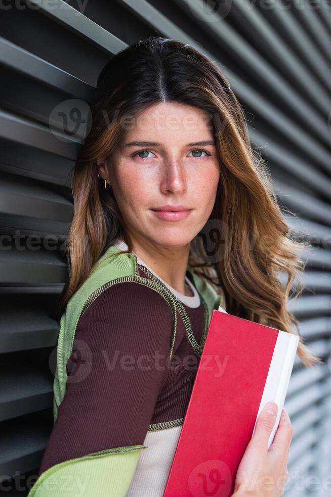 A woman holding a book and standing in front of a wall photo