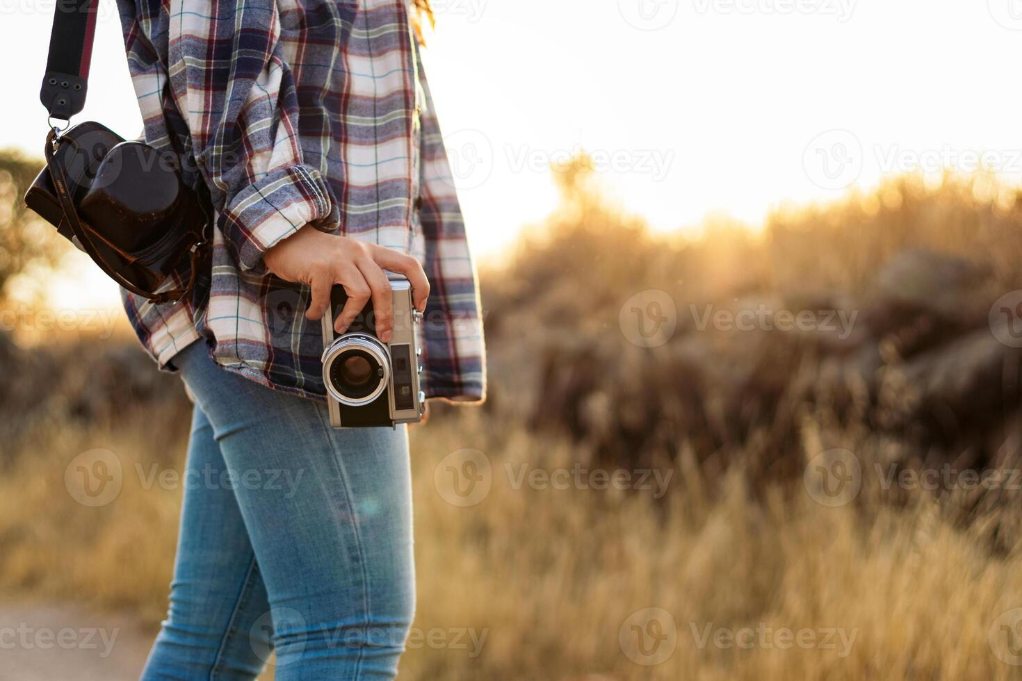 A woman with a camera and plaid shirt standing on a dirt road photo