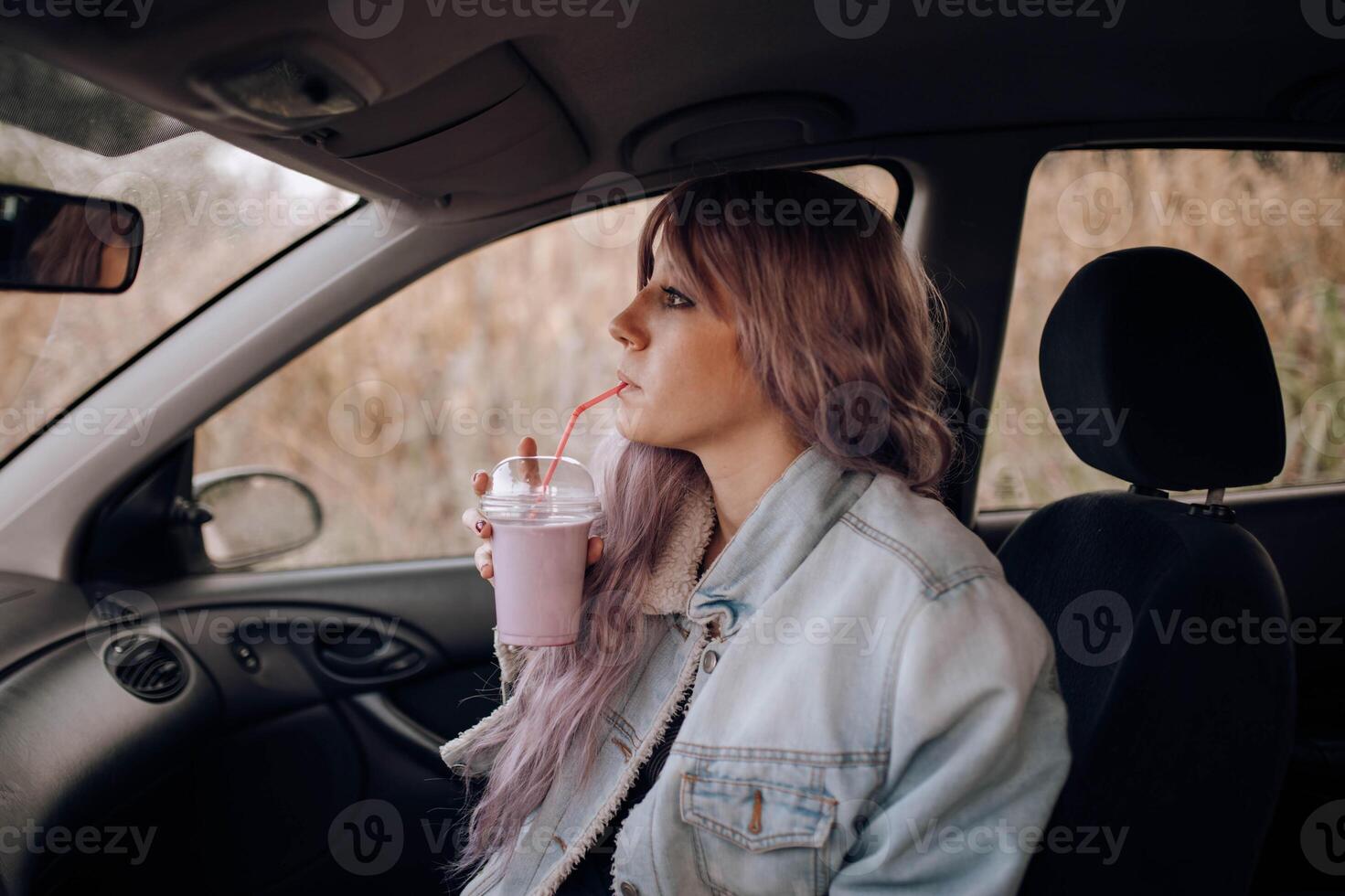 A woman with purple hair sitting in the back seat of a car drinking a smoothie photo