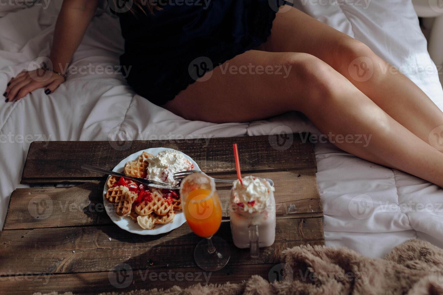 A woman in a black dress sitting on a bed with a tray of food photo