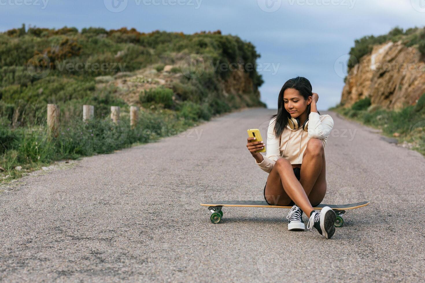 A woman sitting on a skateboard with her phone photo