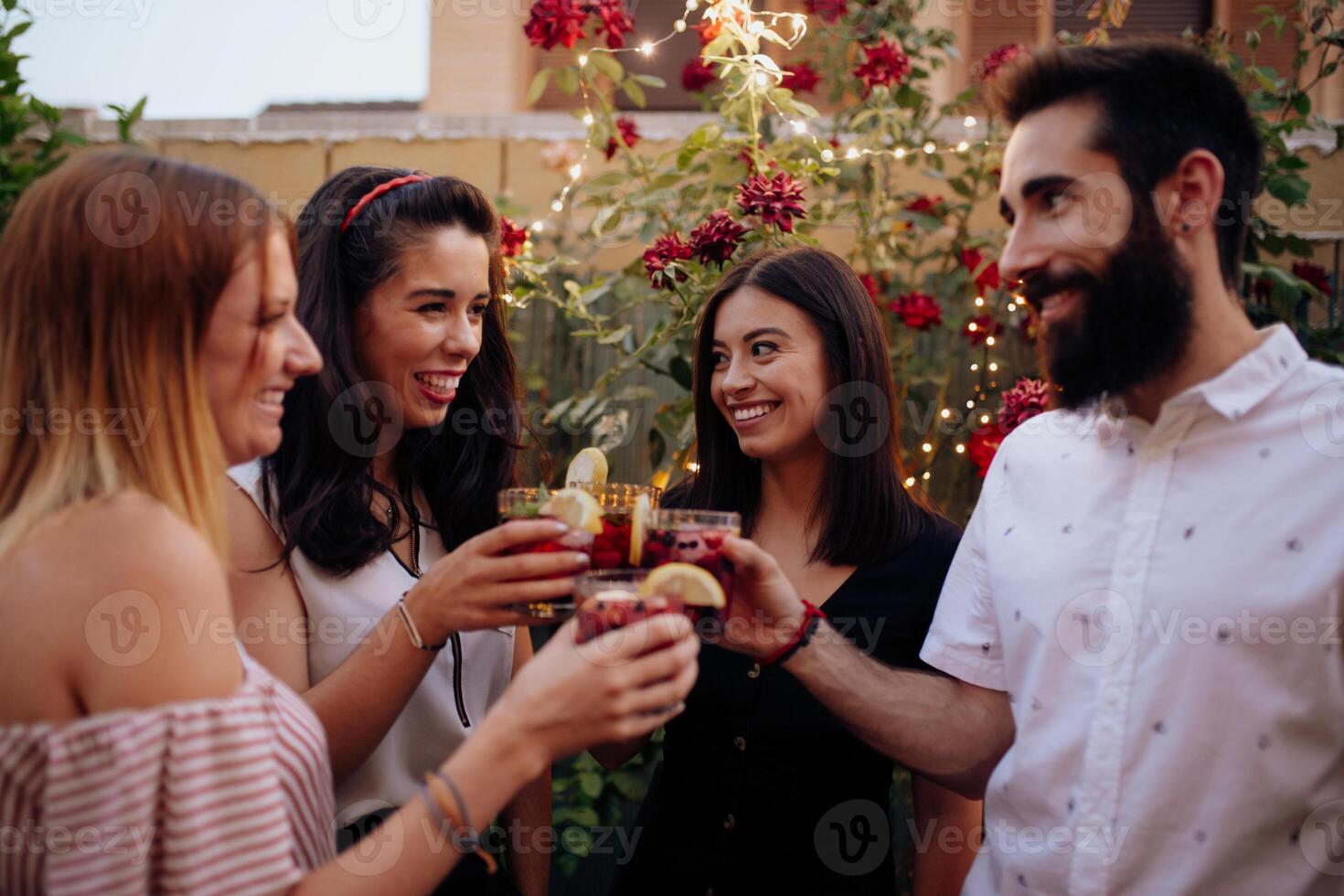 Four friends toasting with drinks in front of a garden photo
