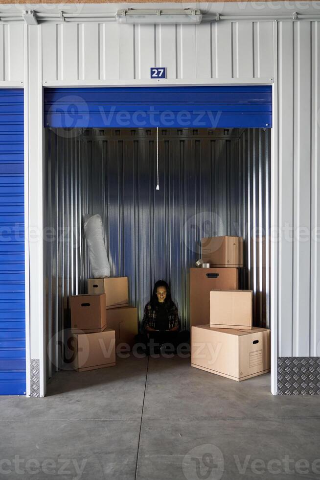 A storage unit with boxes and a man sitting in the doorway photo