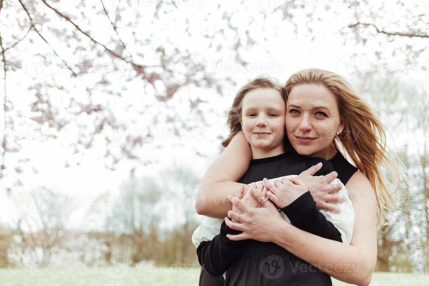 A woman and her daughter hugging in front of a tree photo