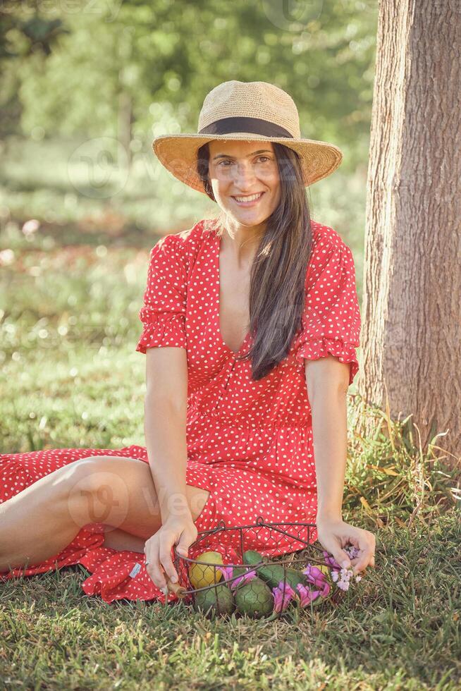 A woman in a red dress and hat sitting on the grass photo