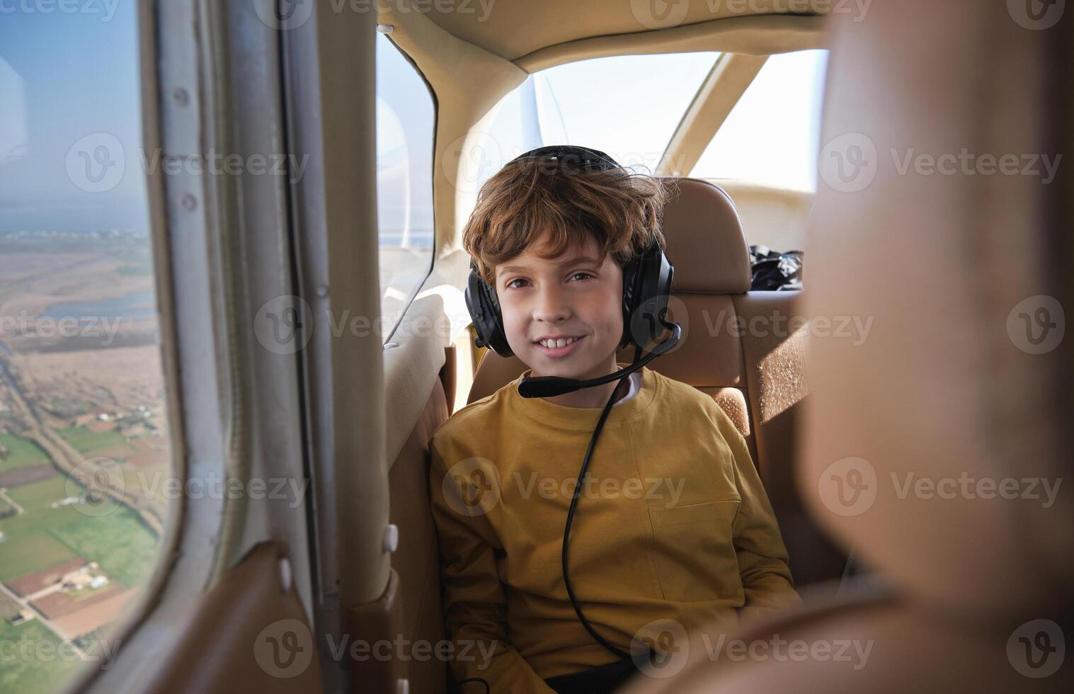 A young boy wearing headphones sits in the cockpit of an airplane photo
