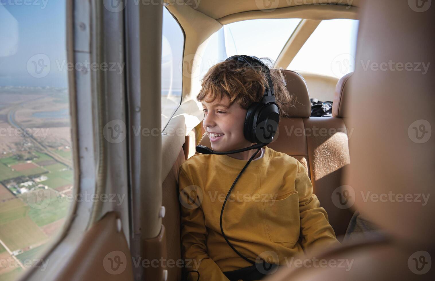 A boy wearing headphones sits in an airplane photo
