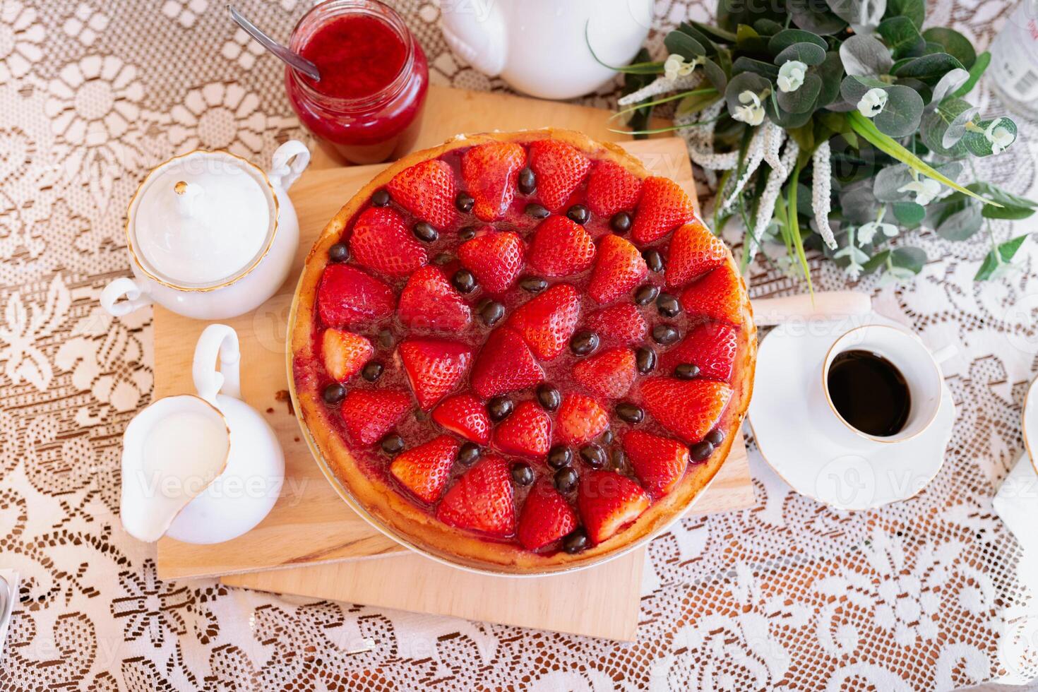 A strawberry pie on a table with a cup of coffee and a plate of cookies photo
