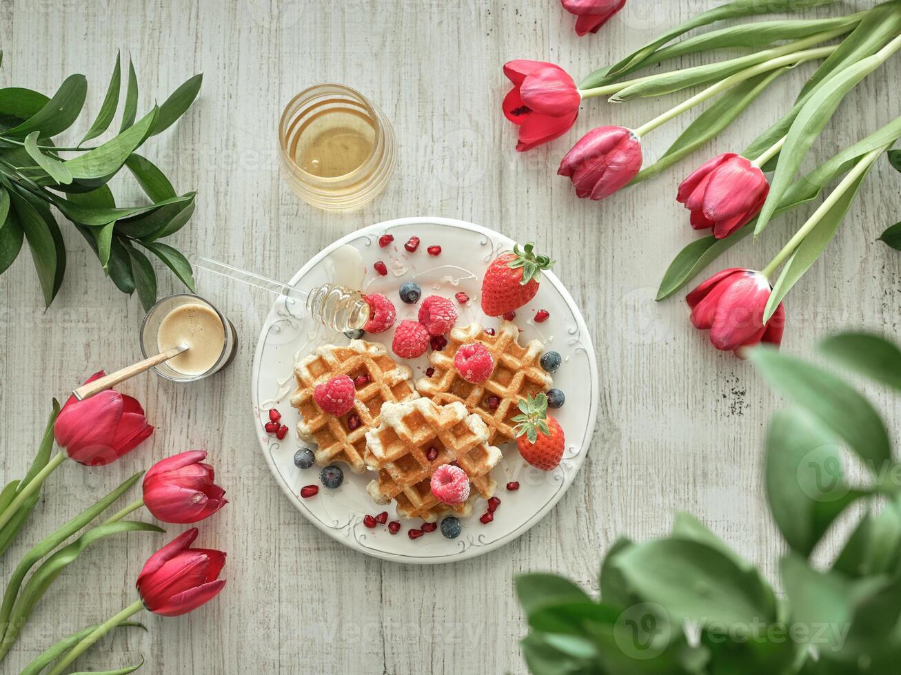 Waffles with berries and honey on a white table with red tulips and red roses photo