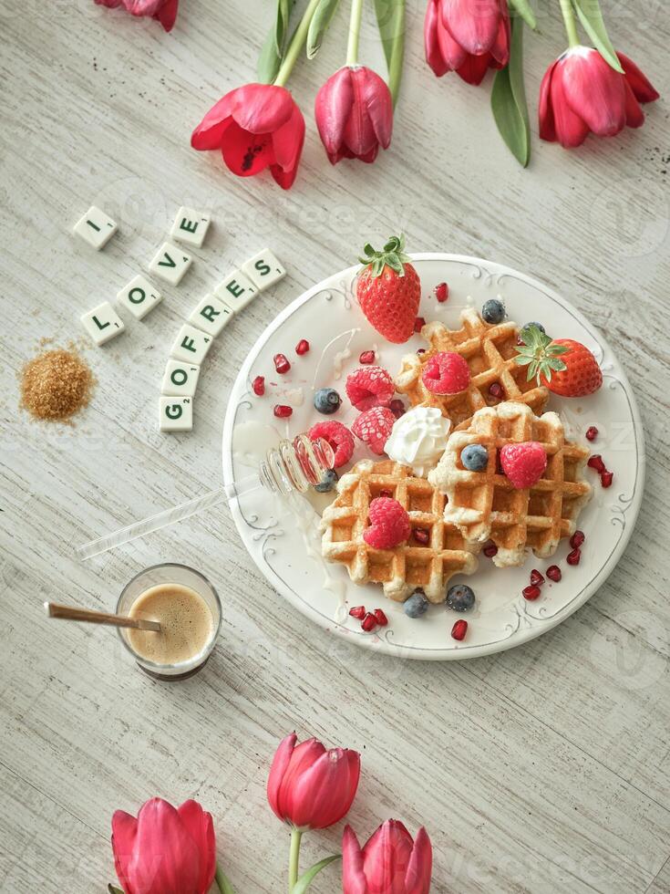 Waffles with berries and honey on a plate with red tulips photo