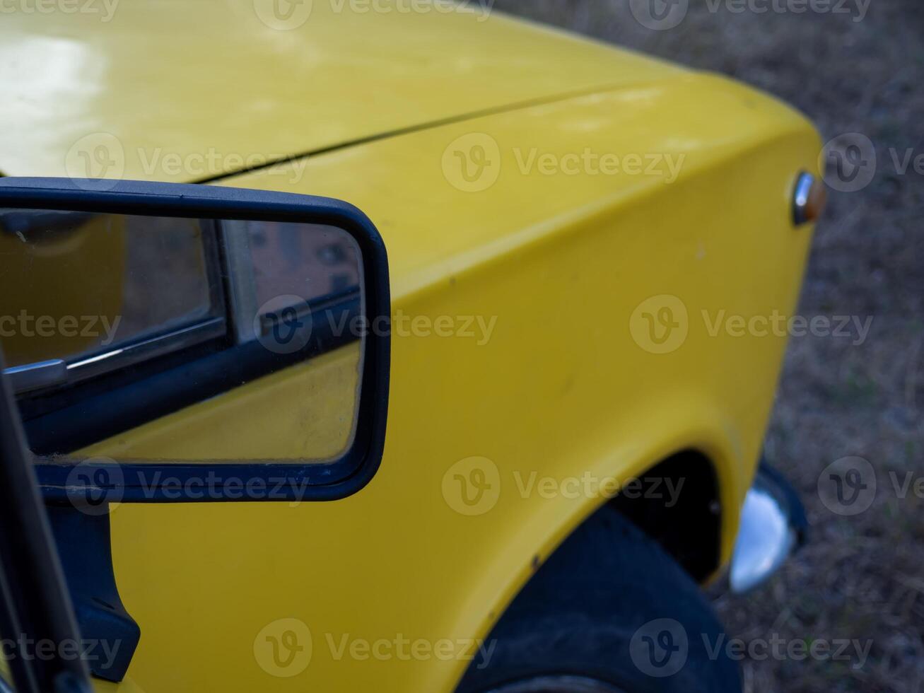 Yellow vehicle parked on grass showing side mirror and part of the front fender in an outdoor setting during daylight photo