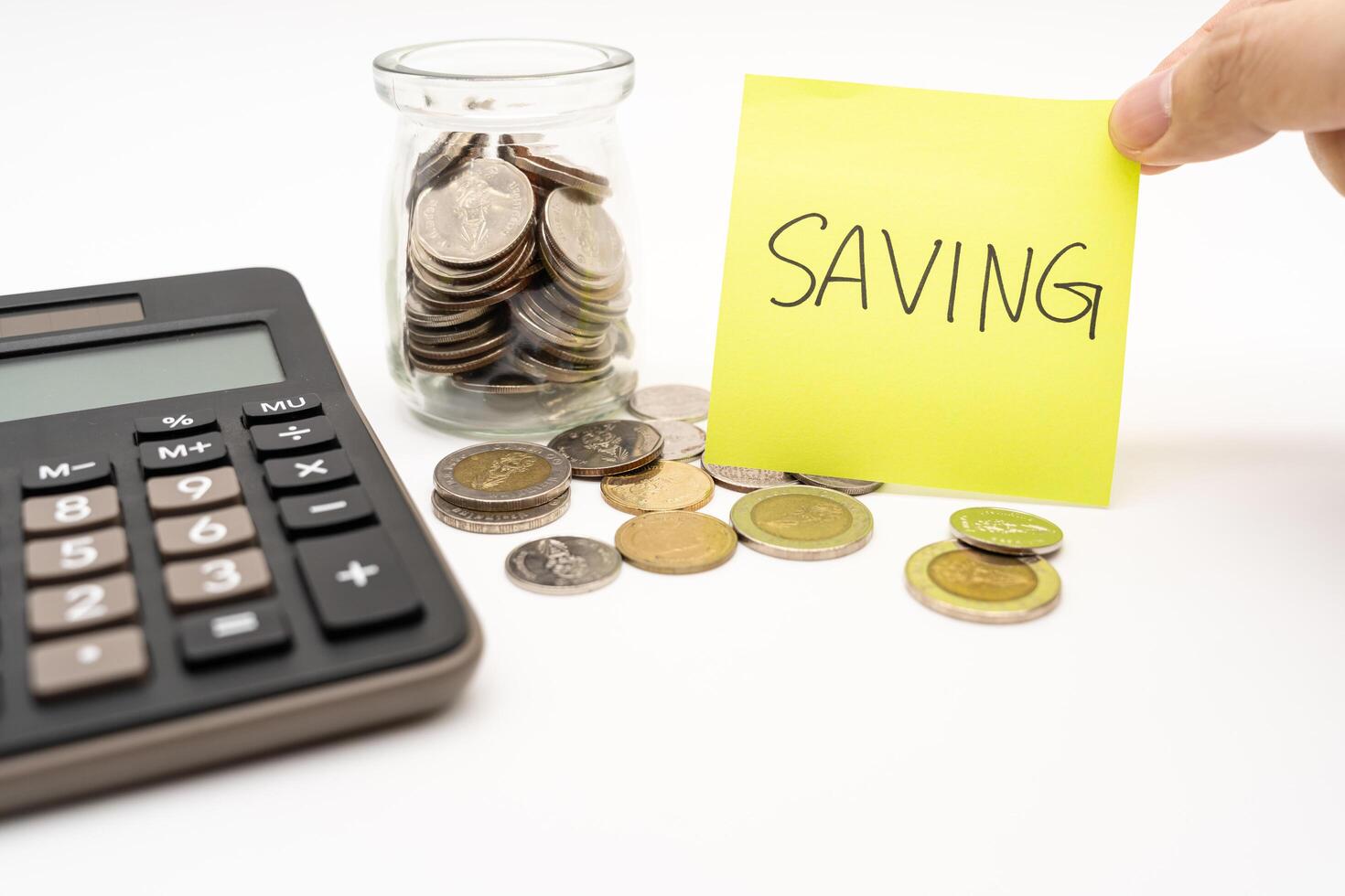 Saving money concept with SAVING text on sticky note. Commitment to achieving financial goals. isolated on white background. Thai Baht Coins spilled out with Calculator. photo