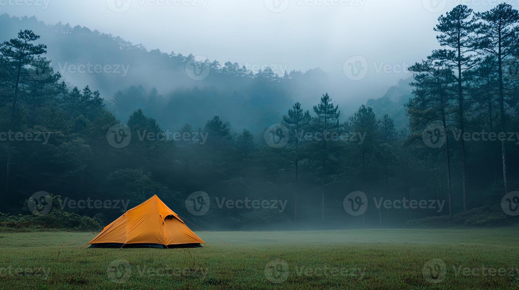 Orange tent stands solitary in a foggy field near dense forest showcasing natures tranquility at dawn photo