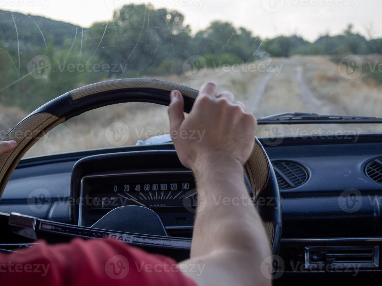 Driving an old car on a dirt road through a scenic countryside landscape during the late afternoon with trees and hills in the background photo