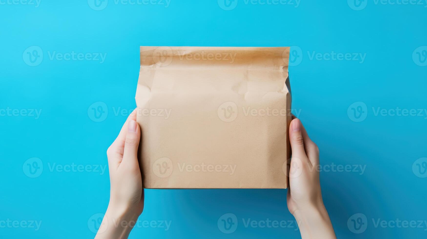 Hands holding a brown paper package on a bright blue background while preparing for delivery or unboxing at home during daytime photo