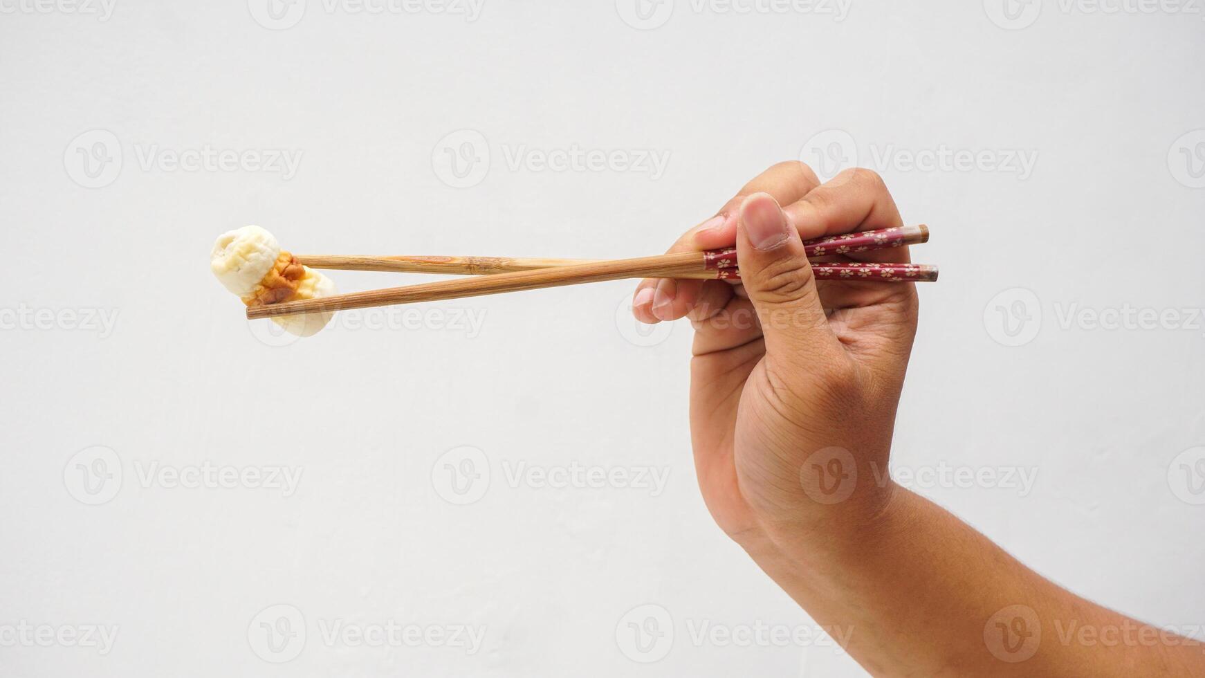 Hand holding wooden chopsticks picked up processed Japanese fish meat or chikuwa isolated on white background photo