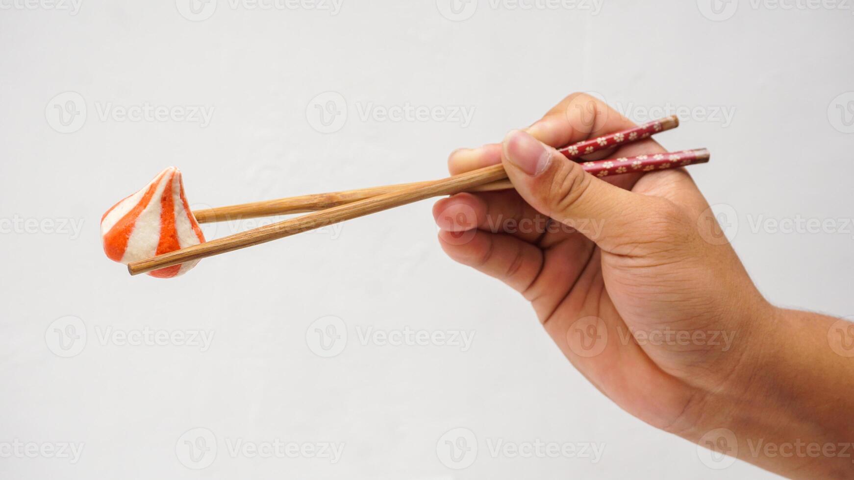 Hand holding wooden chopsticks picked up fish dumpling balls stuffed with chicken meat isolated on white background photo