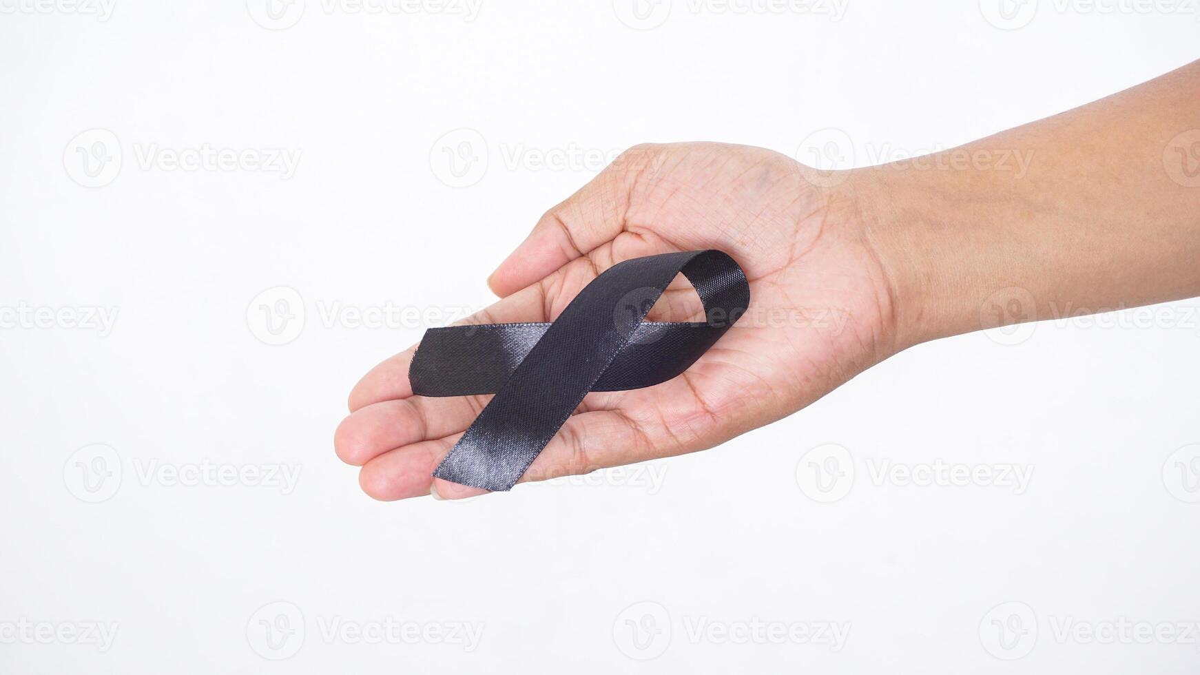 Black ribbon as mourning sign or symbol of melanoma cancer awareness showing in man hand isolated on white background photo