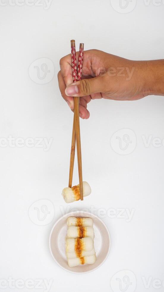 Hand holding wooden chopsticks picked up chikuwa or processed Japanese fish meat isolated on white background photo