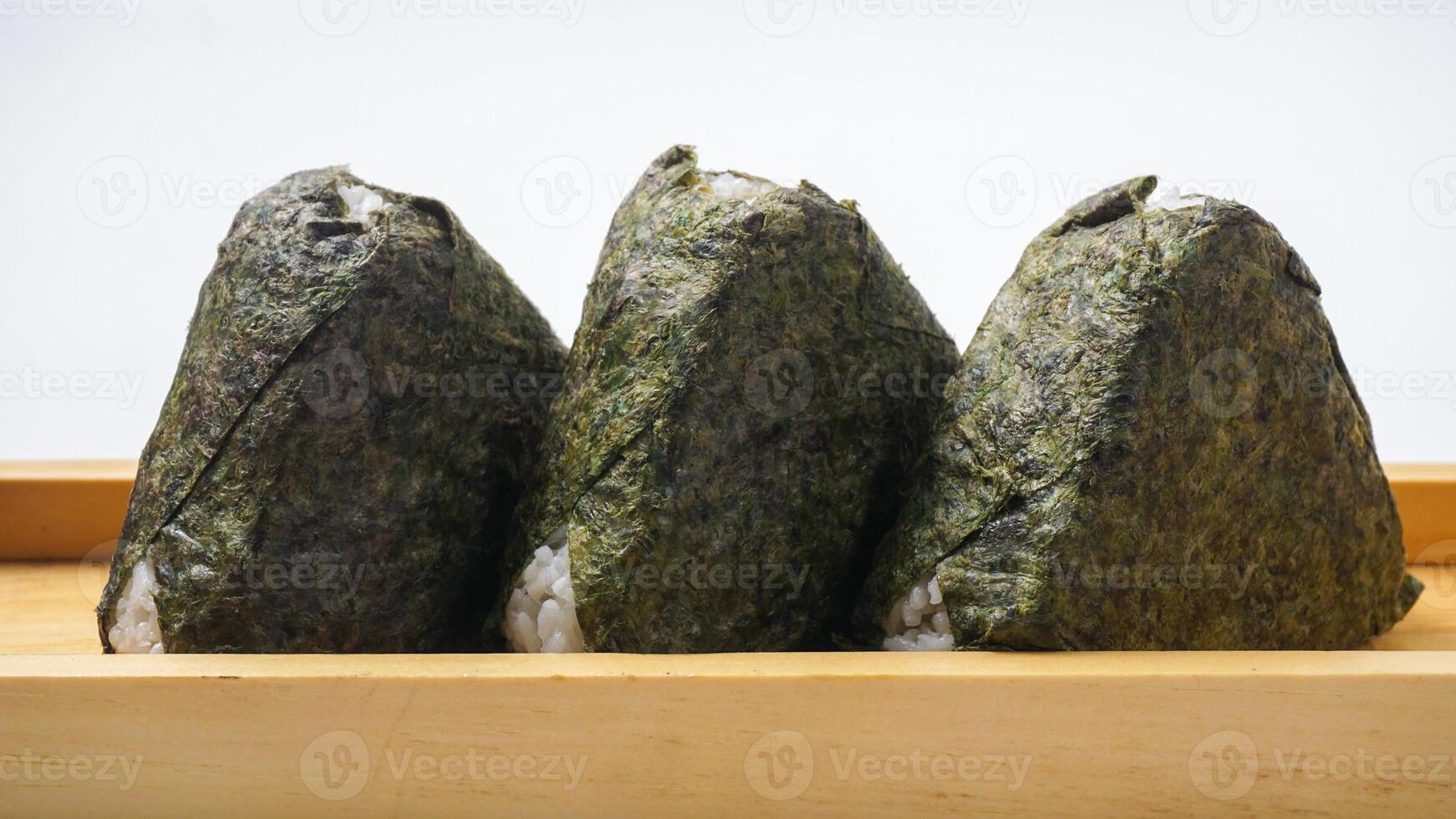 Three Japanese rice ball wrapped in nori dried seaweed or onigiri on wooden coaster isolated on white background photo