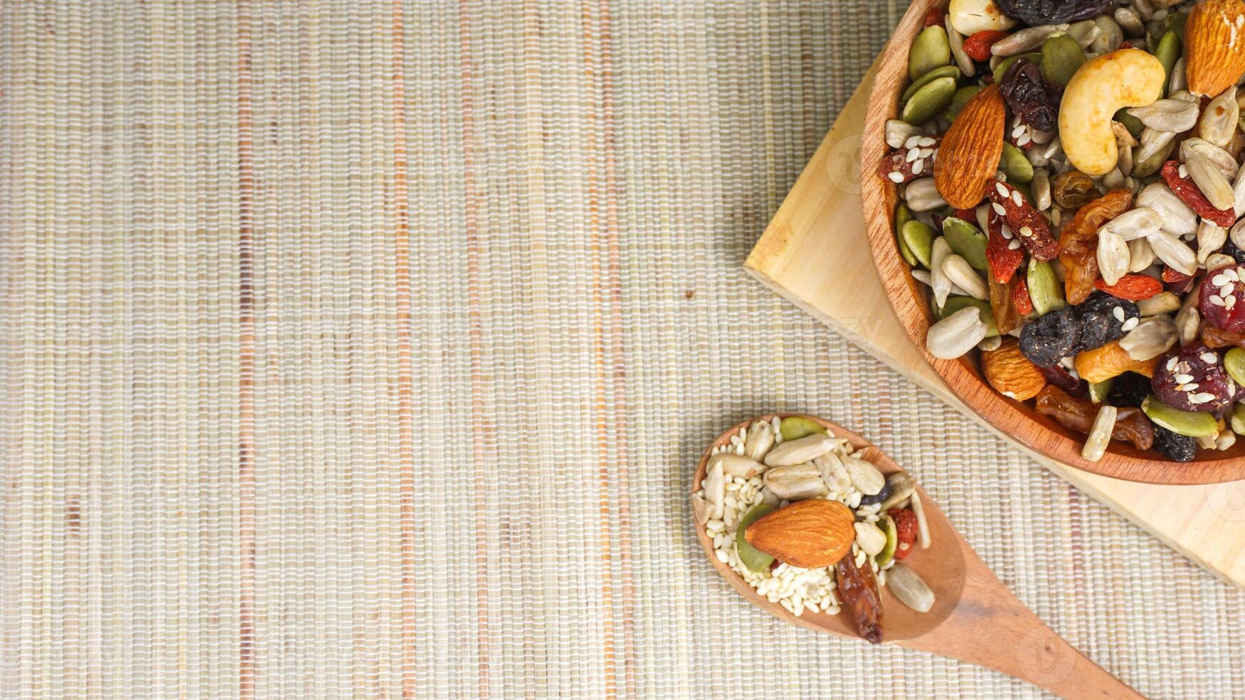 Healthy mix of nuts seeds and dried fruits on wooden plate and spoon isolated on wooden background photo