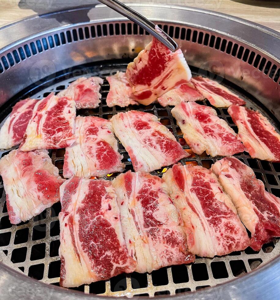 Delicious raw beef slices are being cooked on a grill photo