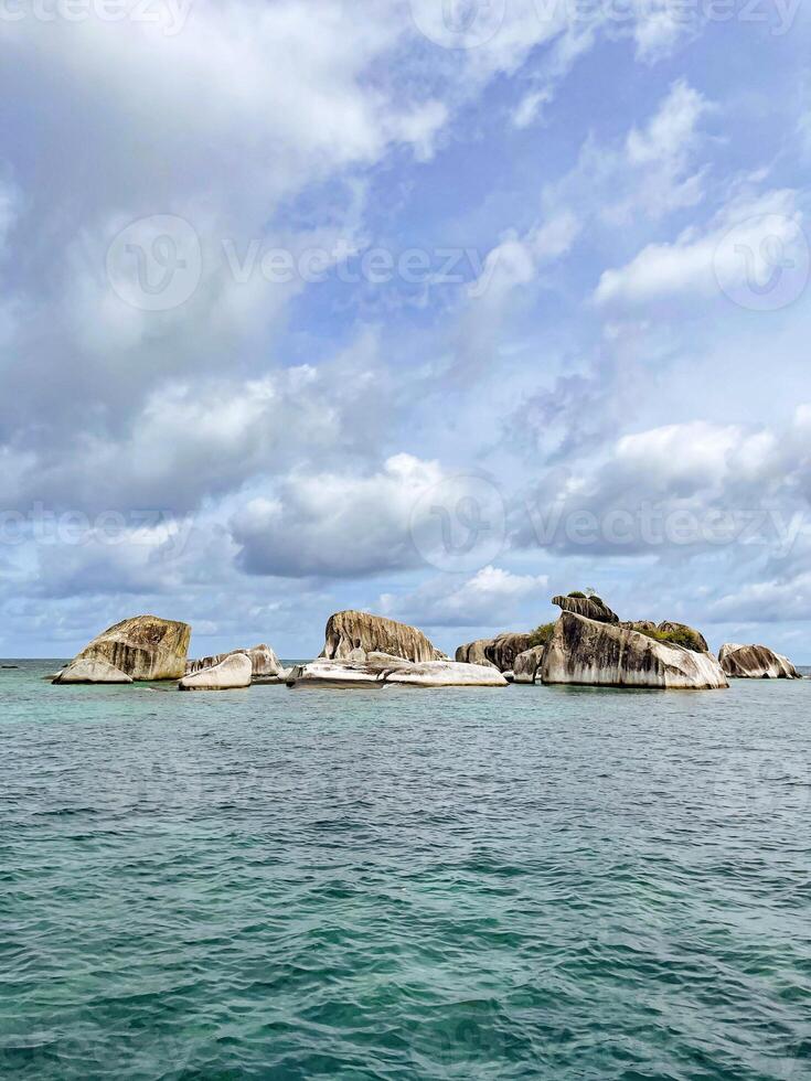 A group of rocks in the ocean with a cloudy sky photo