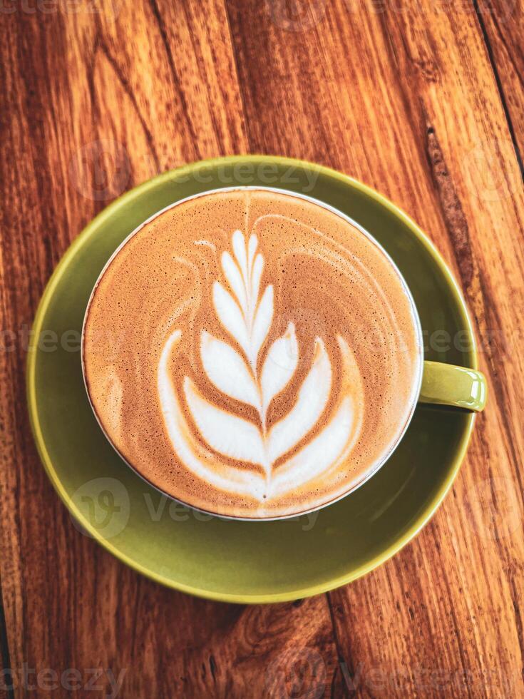 A latte art on a green saucer on a wooden table photo