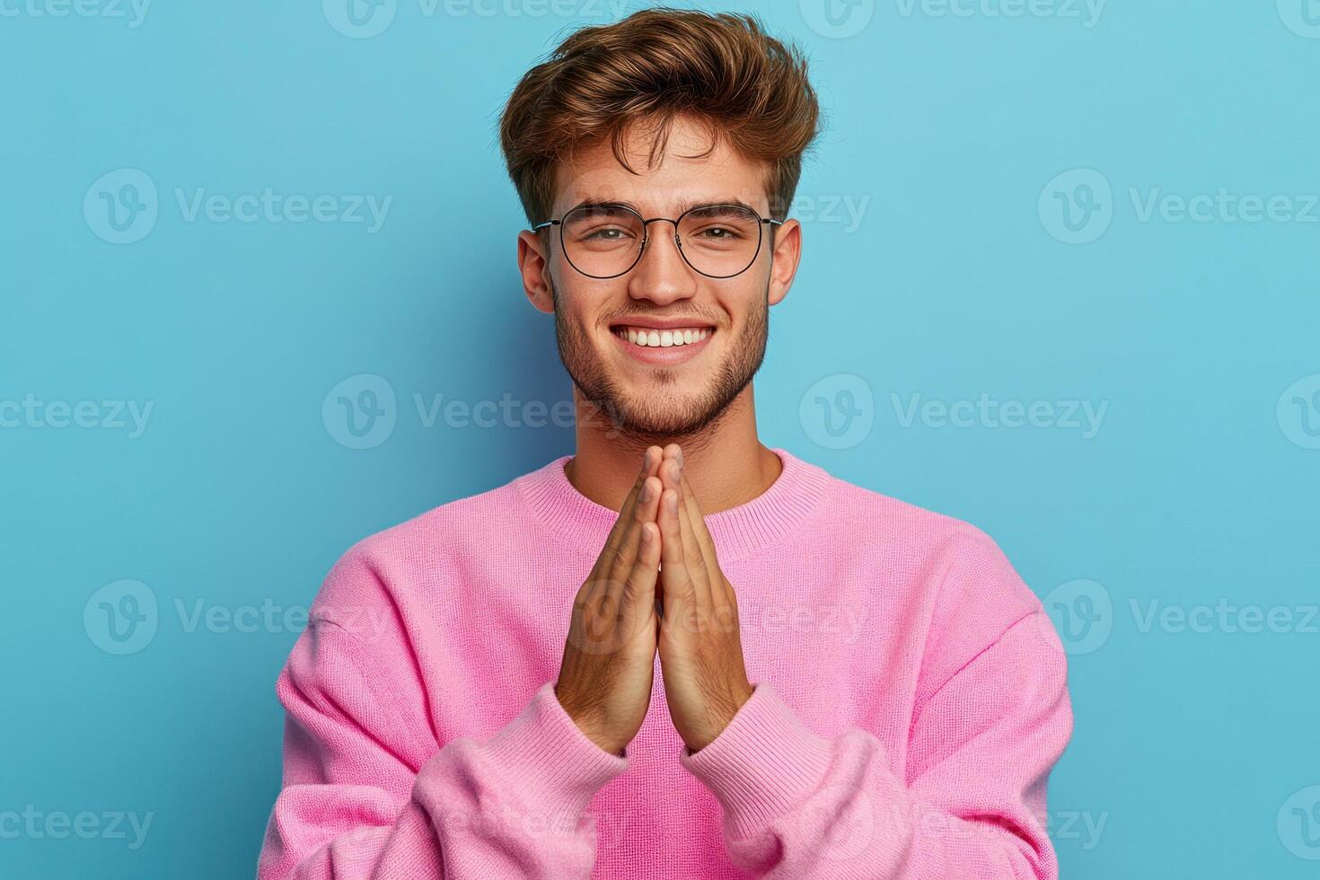Young man smiling with hands together against blue background in casual attire photo