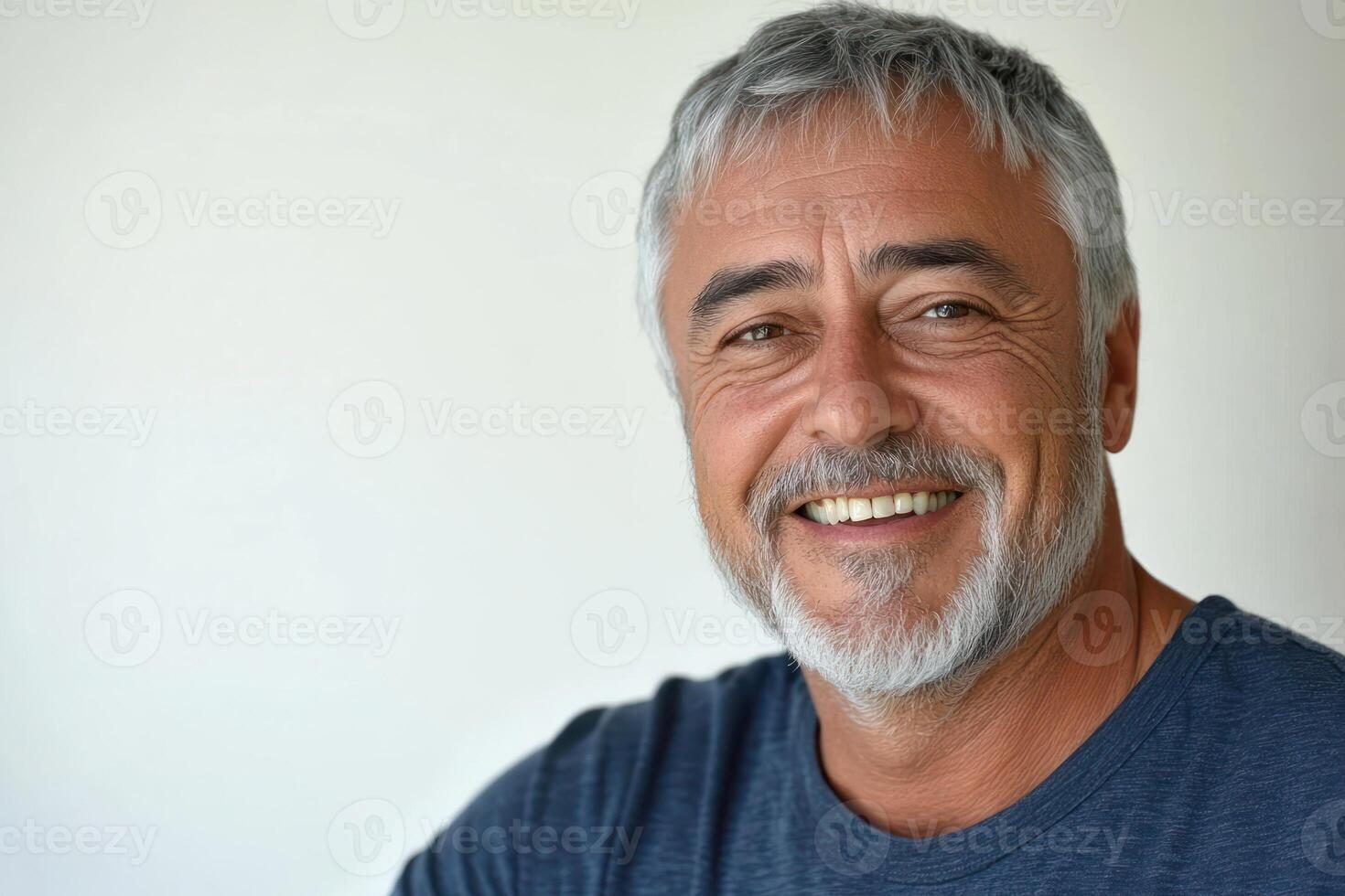 Smiling older man with gray hair and beard in casual attire against a neutral background indoors photo