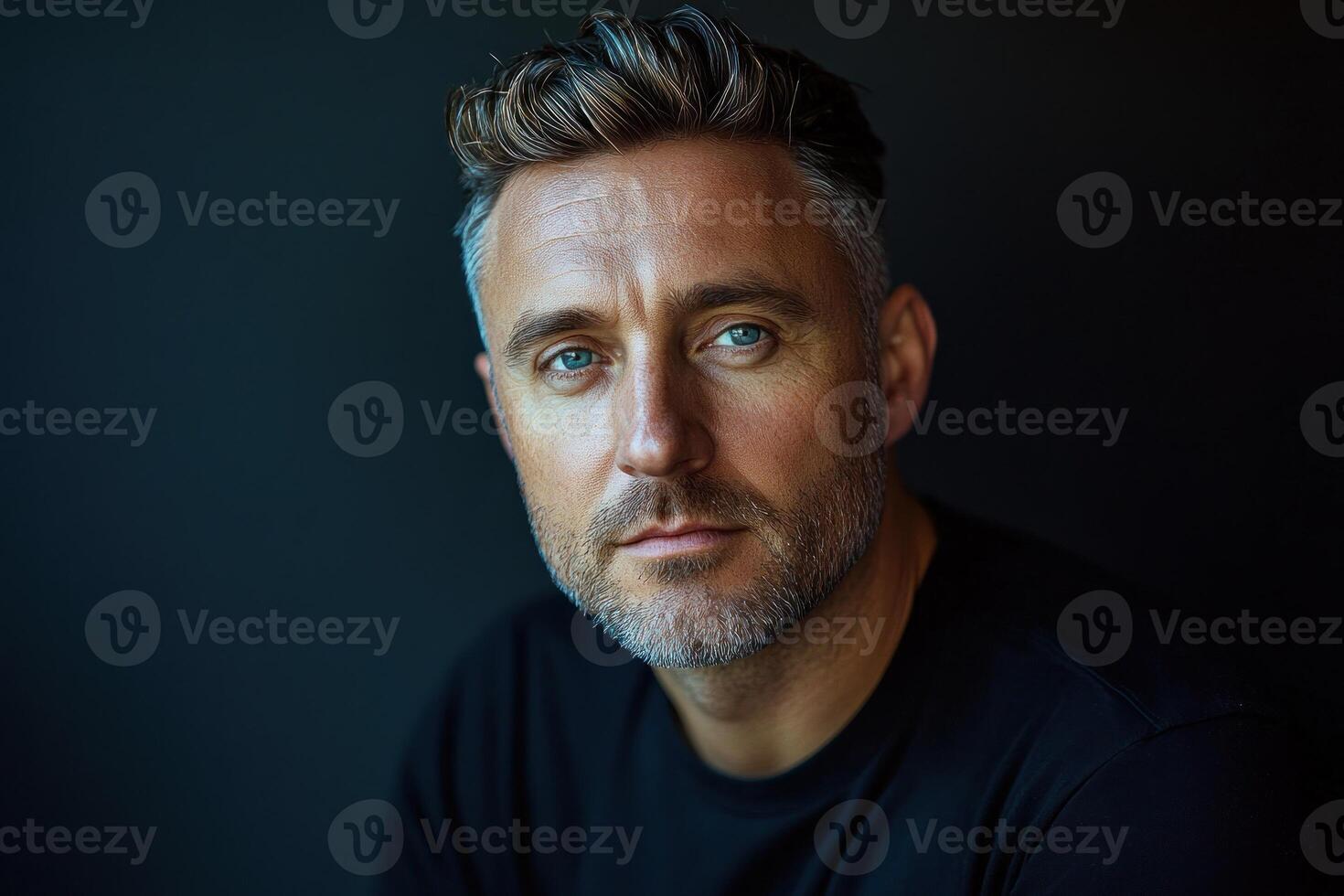 Man with blue eyes and short gray hair poses against a dark background in a simple black shirt photo