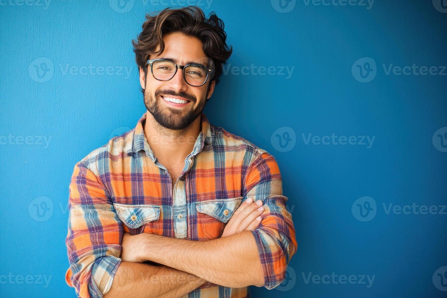 Smiling man in plaid shirt stands confidently against blue wall in indoor setting photo