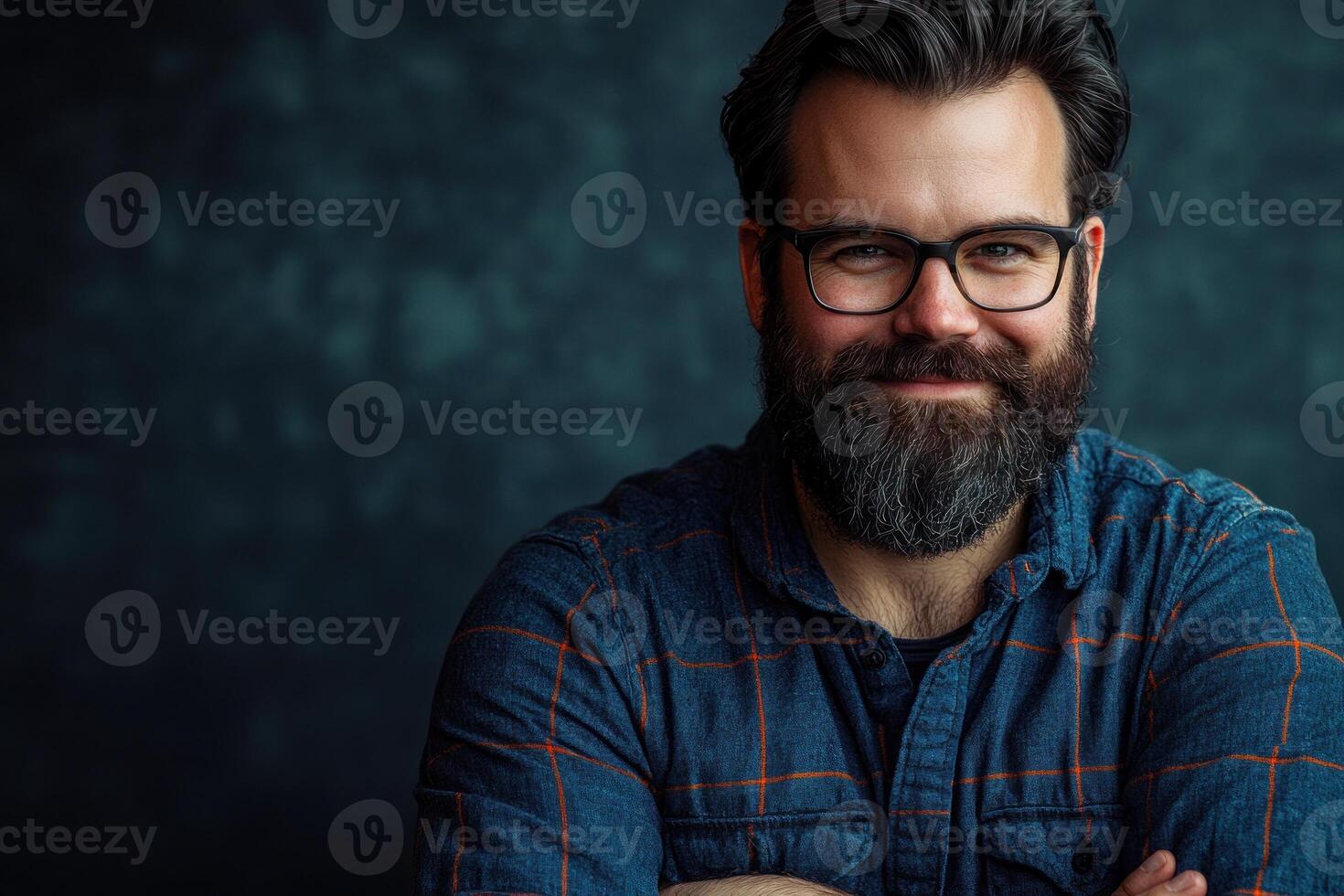 Smiling man with glasses and beard wearing plaid shirt against textured backdrop photo