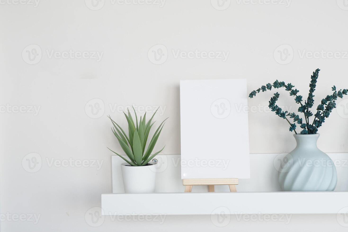 Simple decor with plants and blank canvas on white shelf photo