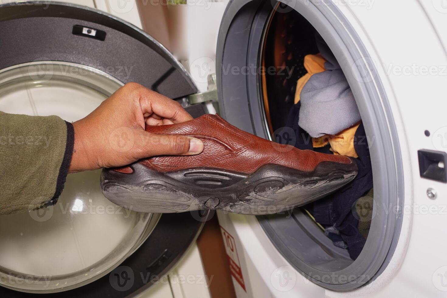 Hand placing a brown shoe into a washing machine photo