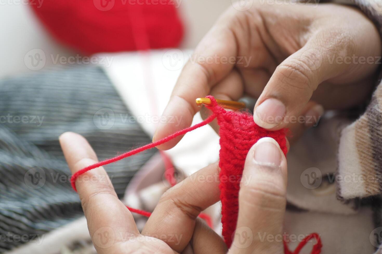 Hands crafting a red crochet piece during a cozy indoor session photo