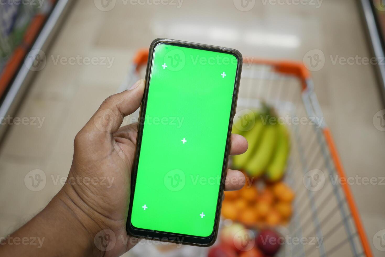Holding a smartphone with a green screen in a grocery store photo