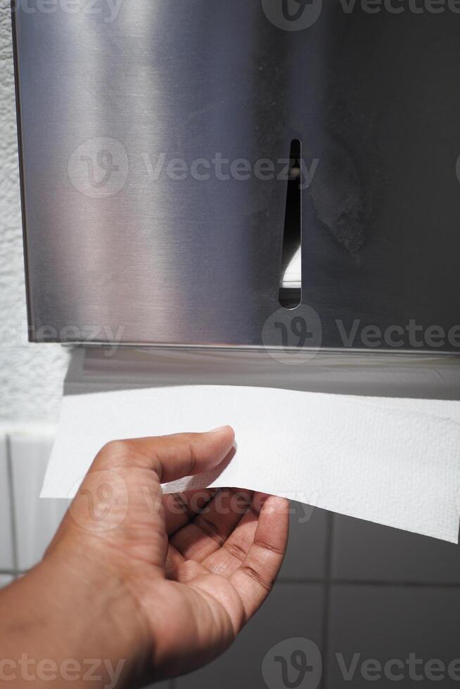 Hand reaching for paper towel from dispenser in a restroom photo