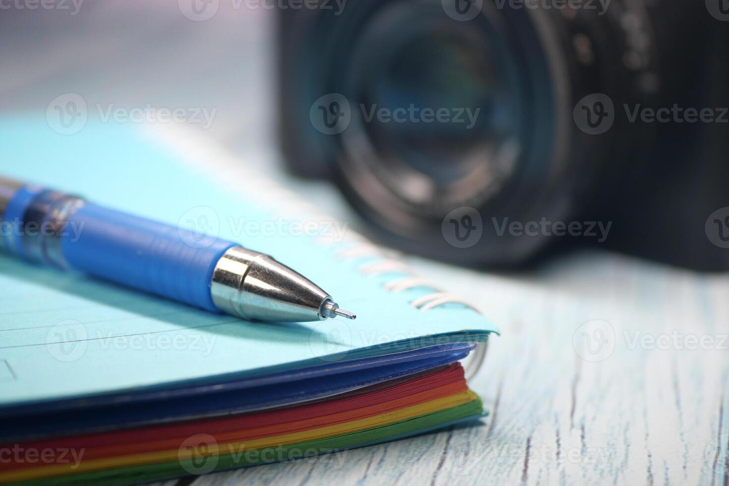 A colorful notebook and pen are placed near a camera on a desk photo