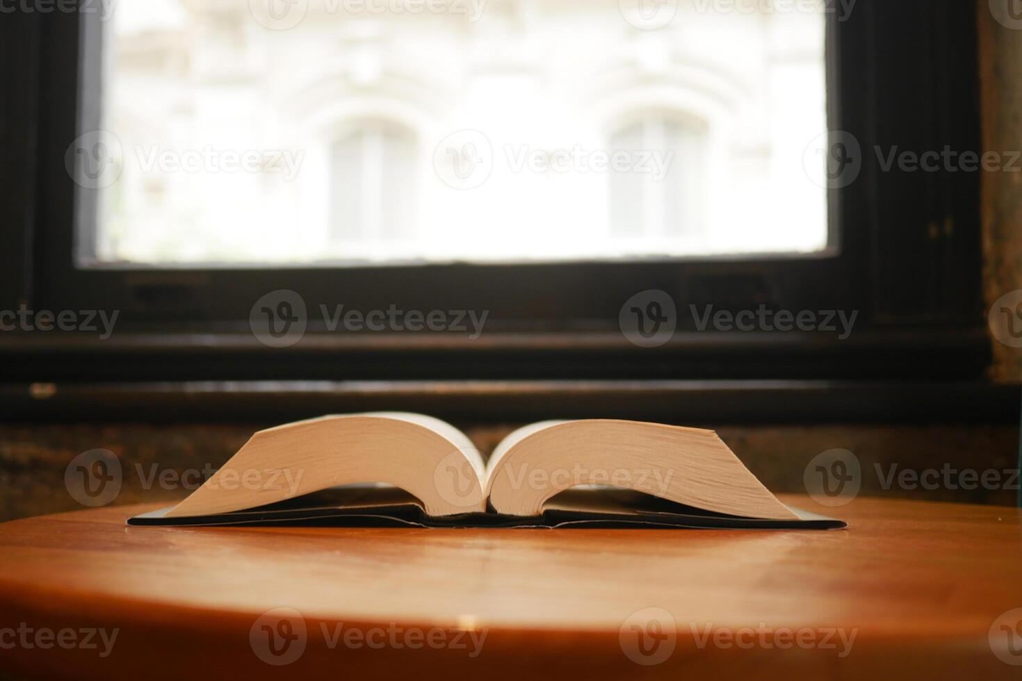 Open book resting on wooden table near large window in a quiet space photo