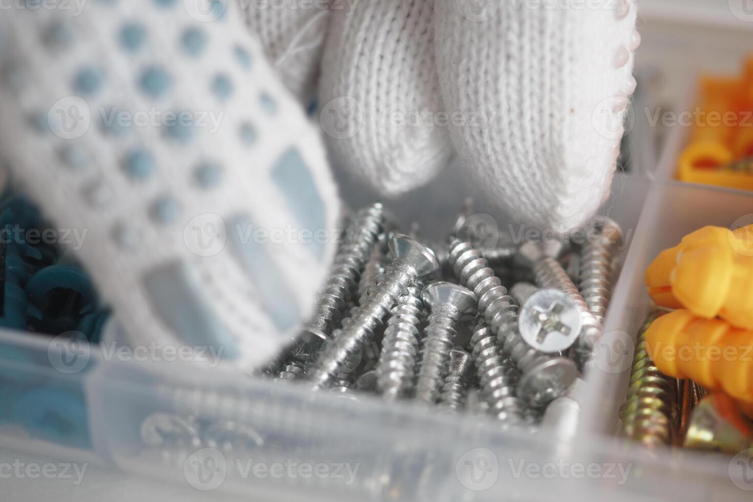 Screws and fasteners sorted in a storage container with gloved hands photo