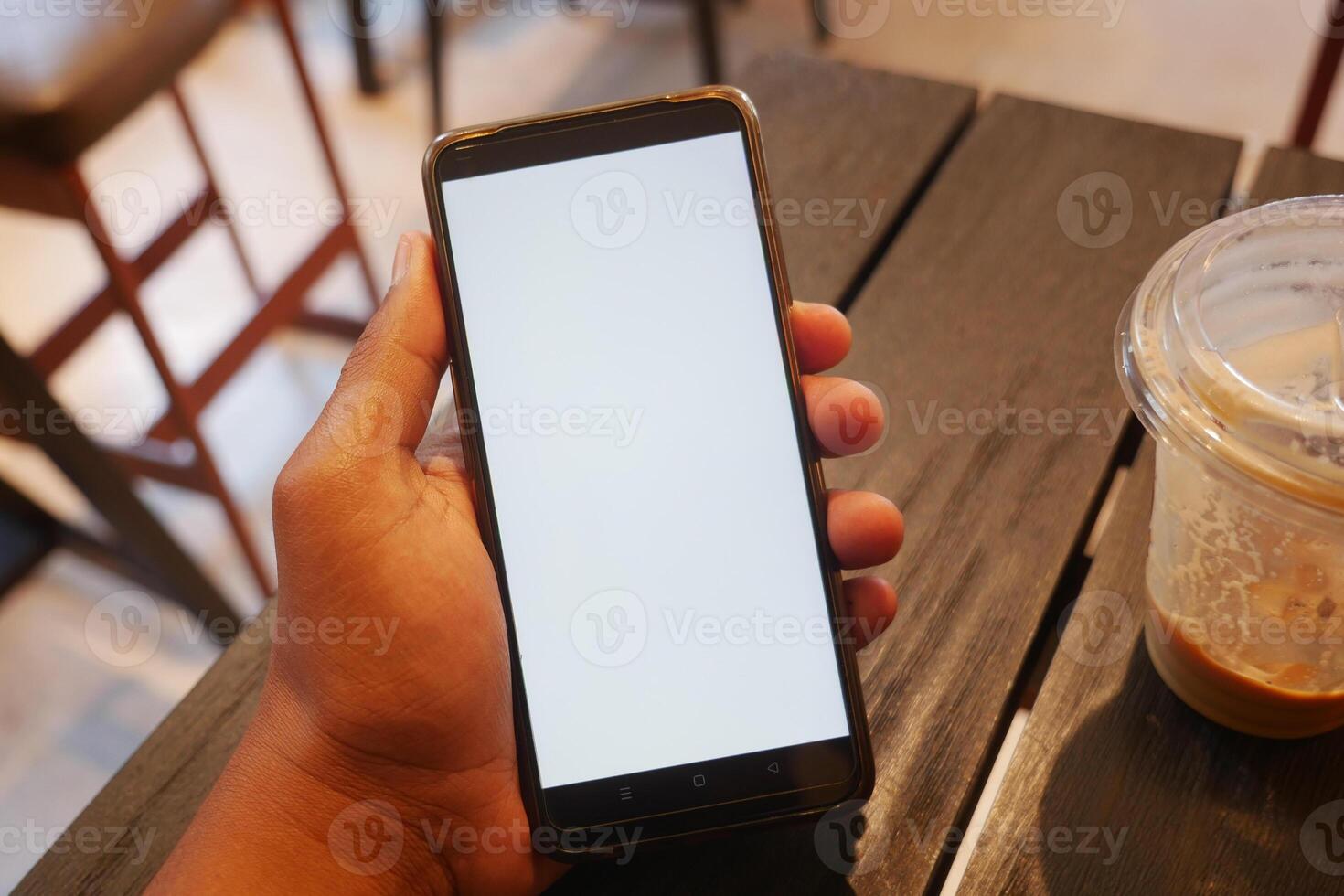 Hand holding a smartphone on a table in a cafe setting photo