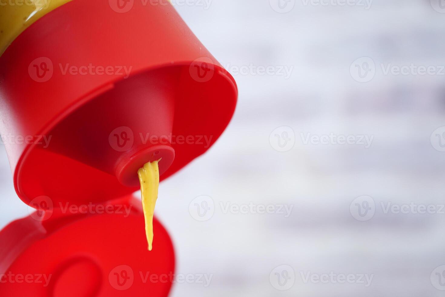 Squeezing mustard from a bottle with a red cap and yellow condiment photo