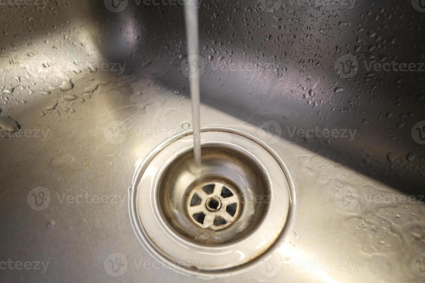 Water flowing into a stainless steel sink drain during a routine wash photo