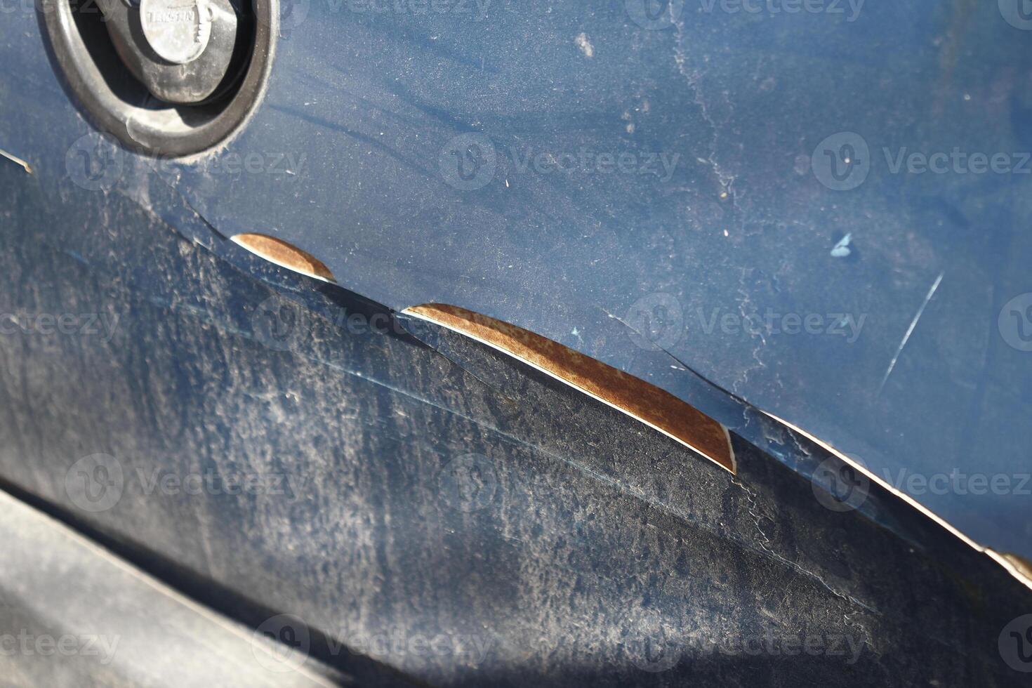 Car paint damage reveals metal underneath in bright sunlight photo