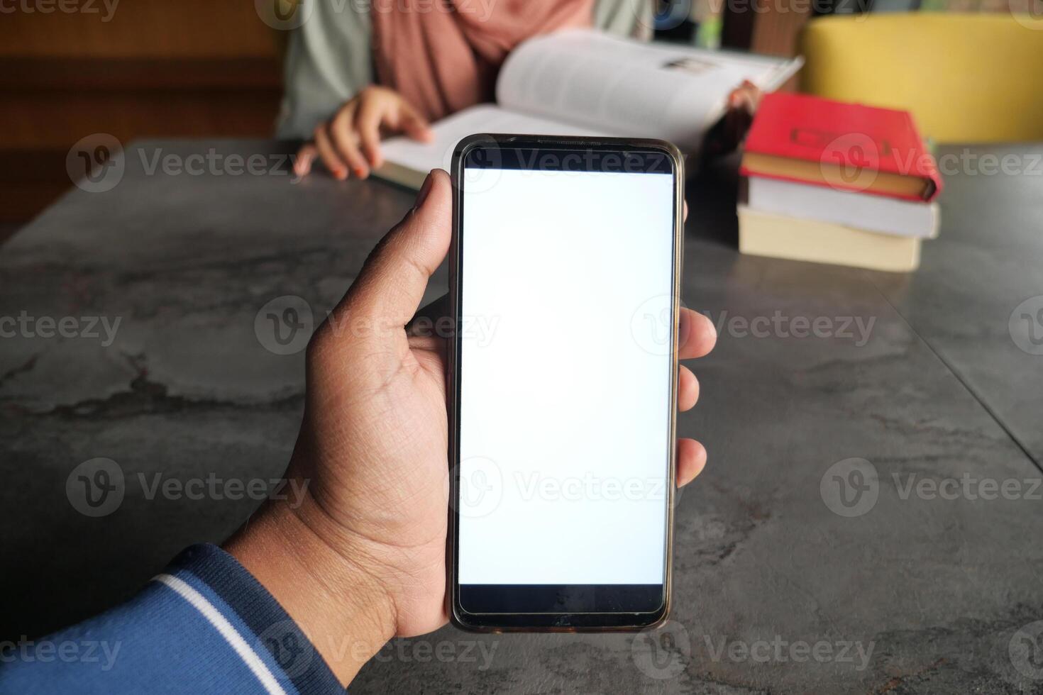 Hand holding a smartphone in a cozy study environment photo