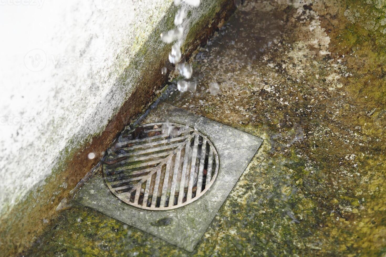 Water dripping from a wall into a metal drain on a concrete surface photo