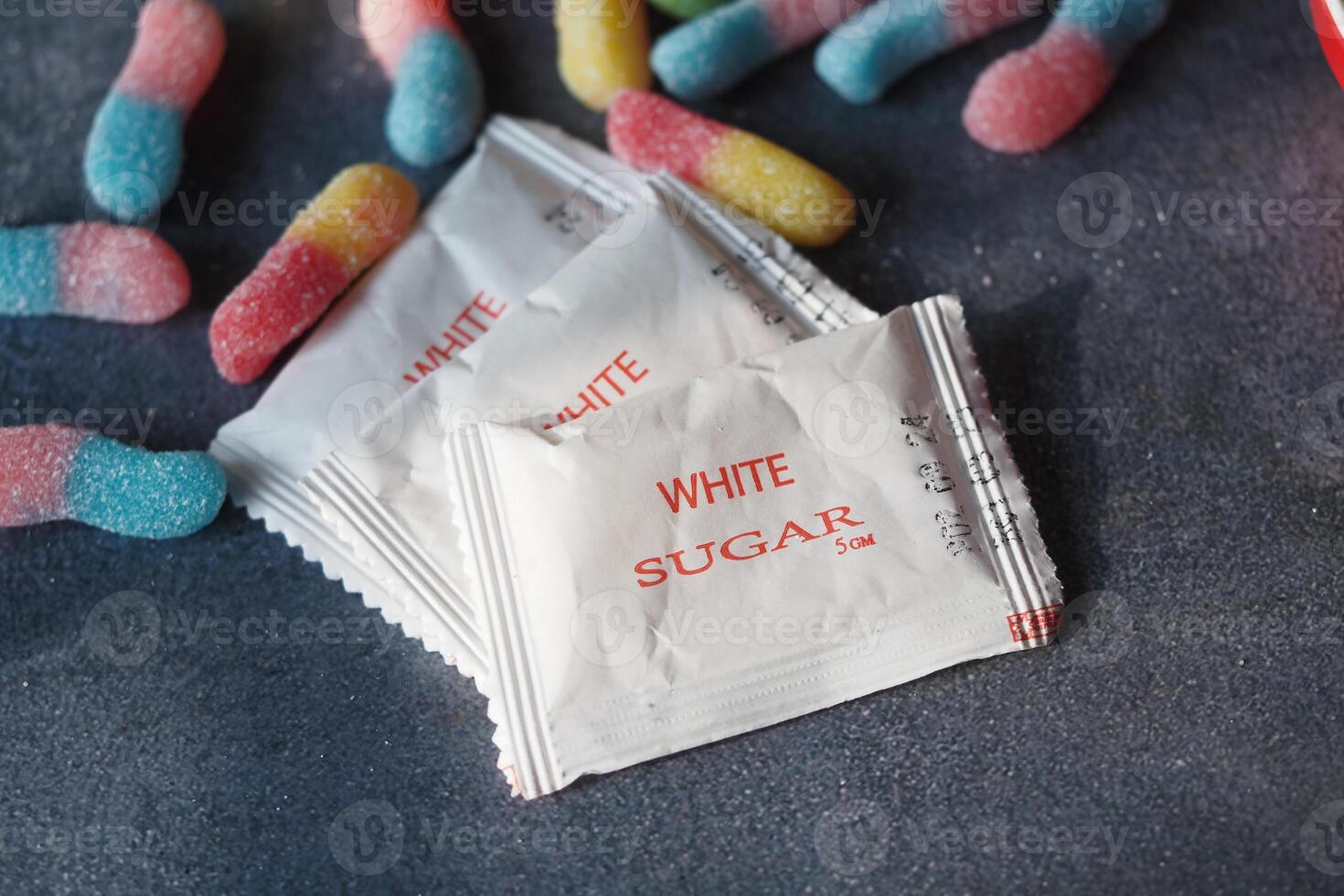 Sugar packets and colorful gummy candies on a dark surface photo