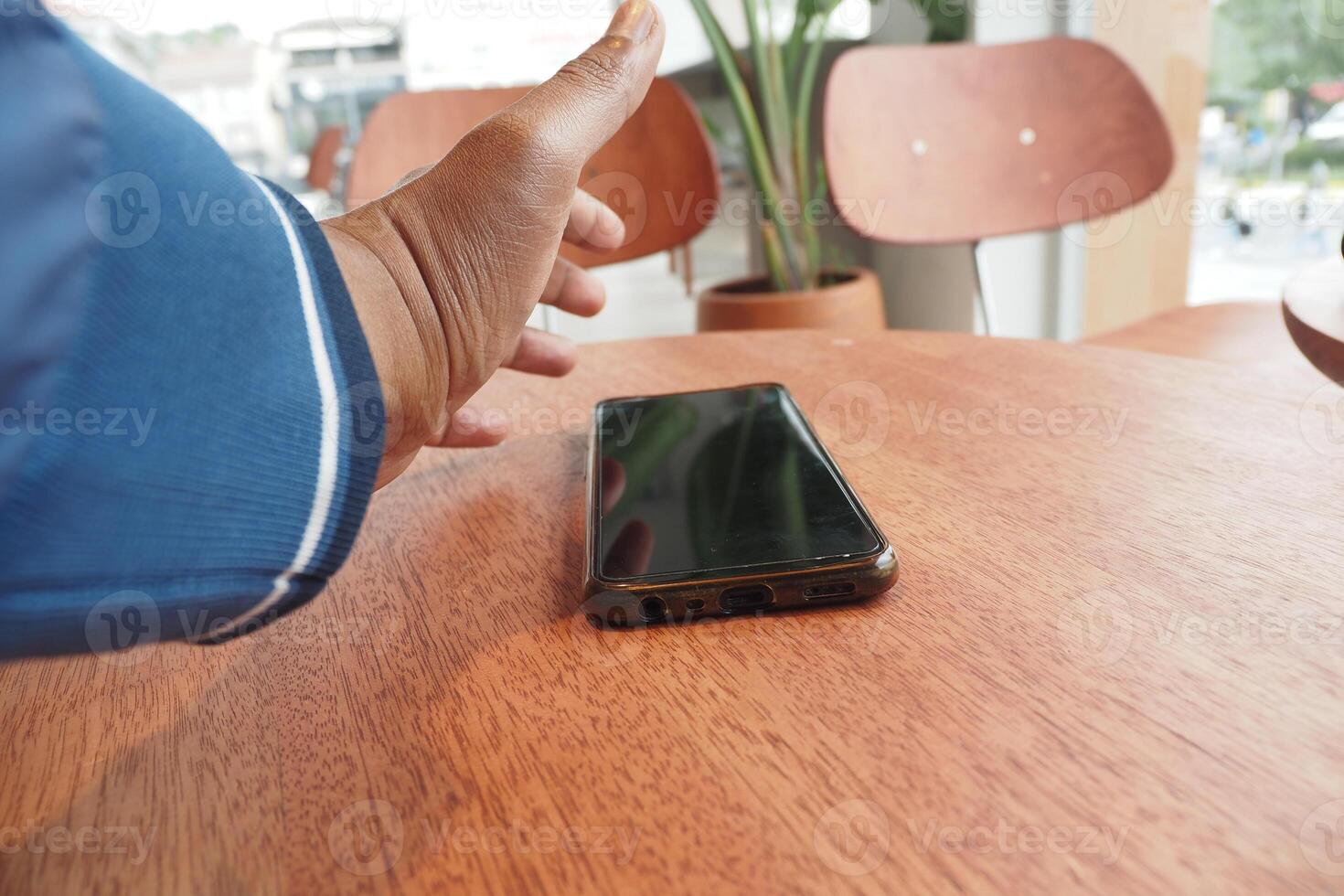 Hand reaching for smartphone on wooden table in a cozy cafe photo