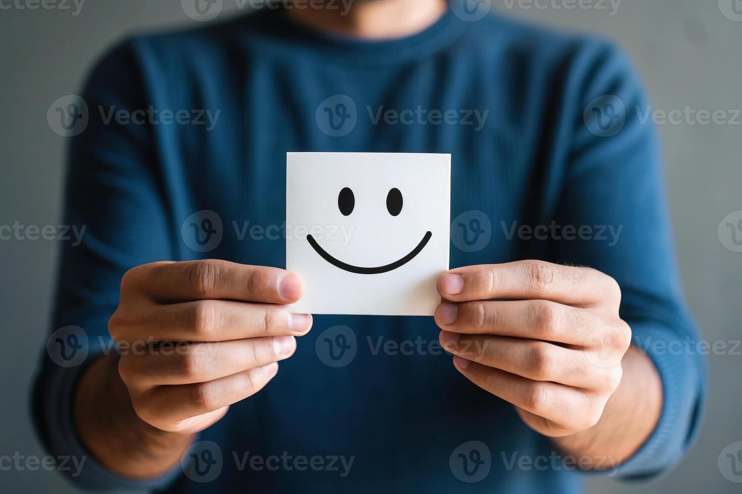A person holds a smiling face on a note, conveying positivity and joy against a neutral background. photo